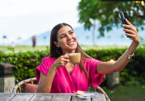 Portrait of smiling russian woman drinking hot capuccino and taking a selfie