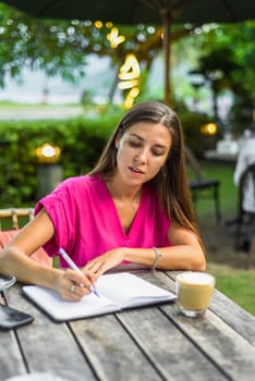 Cute woman sitting on a chair in summer garden and writing in a notebook
