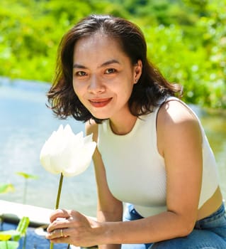 Vietnamese young woman smiling and smelling a white lotus in Vietnam