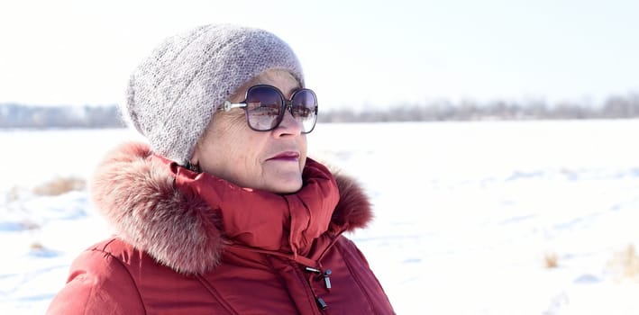 Russian senior woman talking on phone against snowy field. winter