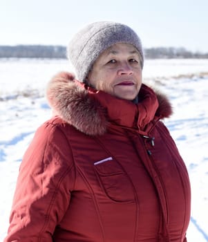Portrait of Russian senior woman in beanie and sunglasses looking away against snowy field. winter