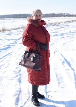 Portrait of Russian senior woman in beanie and sunglasses looking away against snowy field. winter