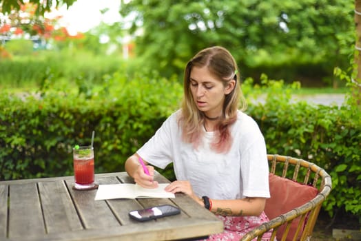 Cute  woman sitting on a chair in summer garden and writing in a notebook