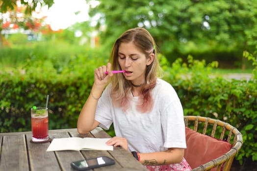 Cute  woman sitting on a chair in summer garden and writing in a notebook