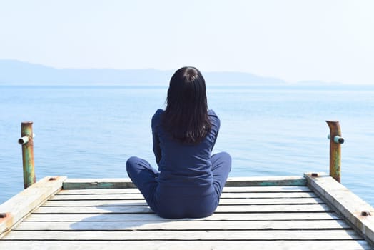 45 y.o. Russian woman sitting in lotus position on a wooden pier against the Japanese sea