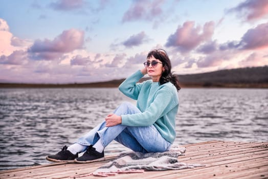 49 year old Russian woman in sweater sitting on a pier and thinking with eyes closed