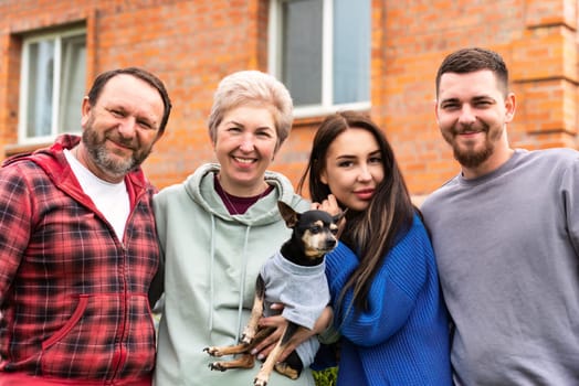 Portrait of happy family together with dog hugging near their  house.