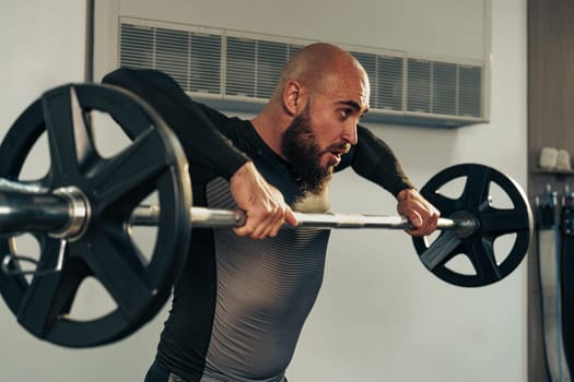 A man with a beard lifts a barbell with weights during a focused workout in a modern gym. The environment emphasizes strength training and dedication to fitness.