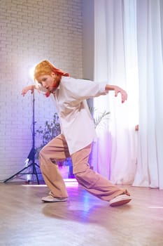 A talented young dancer showcases their skills in a stylish studio with soft lighting. The dancer wears a loose shirt and pants, striking an energetic pose on wooden flooring.
