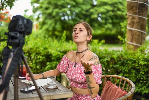 Cute videographer and vlogger taking a video with camera and tripod in summer garden