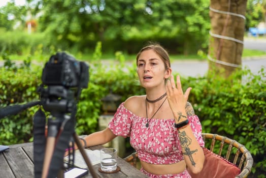 Cute videographer and vlogger taking a video with camera and tripod in summer garden