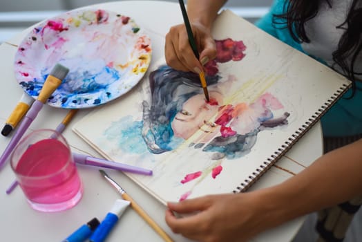 Woman painting watercolor drawing of asian girl with brush on a table with water and paints