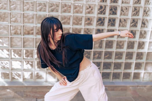 A young woman performs dynamic dance moves in an urban setting, wearing casual attire. Sunlight highlights her energetic expression and stylish form, creating a lively atmosphere.