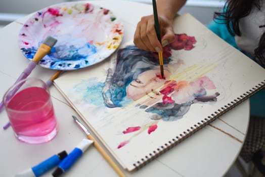 Woman painting watercolor drawing of asian girl with brush on a table with water and paints