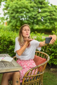 Cute woman taking a photo selfie and blowing a kiss in summer garden