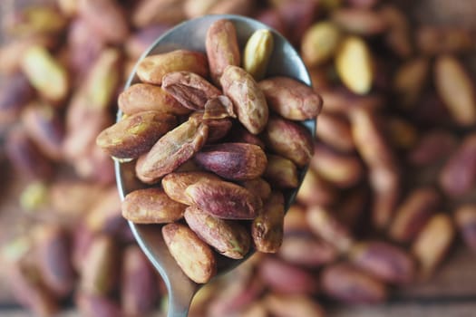 A spoonful of roasted nuts is placed over a rustic wooden surface.