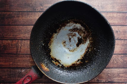 An old frying pan sits on a weathered wooden table, revealing its age.