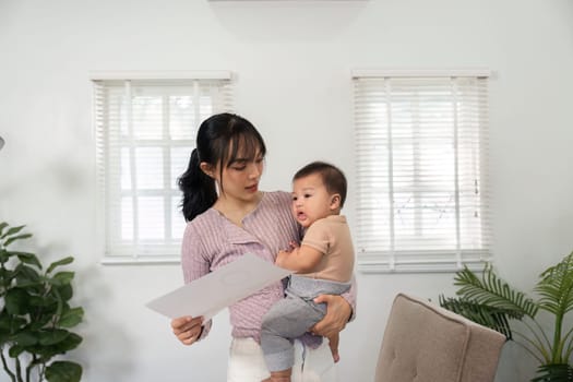 A focused mother discusses project details with her baby in her arms, showcasing her commitment to both parenting and professional responsibilities in a bright home office.
