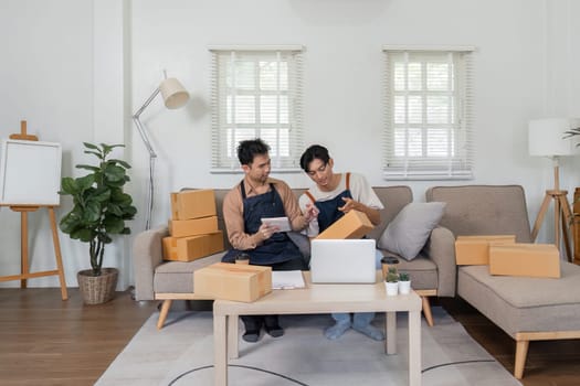 Two men, in a cozy living room, working together to pack orders for their online business, showcasing teamwork and entrepreneurship.