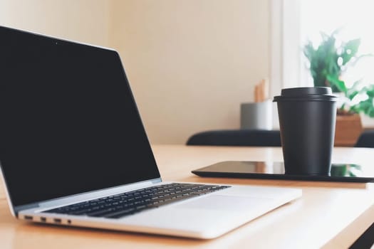 A sleek laptop and a coffee cup sit on a wooden table, creating a cozy workspace vibe. A tablet is nearby, enhancing the modern minimalist aesthetic.