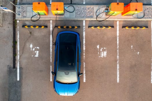 Top view of blue electric car receives electricity at public charging point. Parking lot equipped with plugs and connectors for quick replenishing of energy