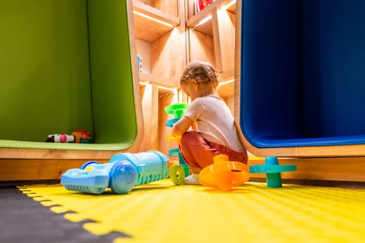 Toddler playing with a toy vacuum cleaner and exploring shelves in a bright and colorful playroom