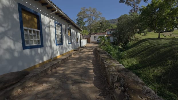 A video of a stroll down a cobblestone street in a vibrant colonial Brazilian village, featuring lush nature on the opposite side.