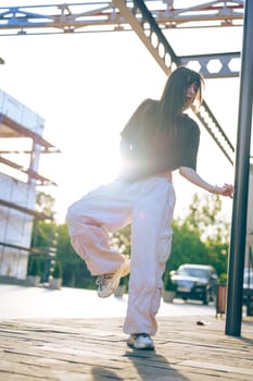 A young woman performs a dance move outdoors at sunset, surrounded by early construction. The warm light creates a captivating atmosphere as she enjoys her moment.