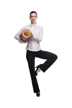 Full body fit lady in formal wear carrying rolled up mat and balancing on leg during yoga workout against while background