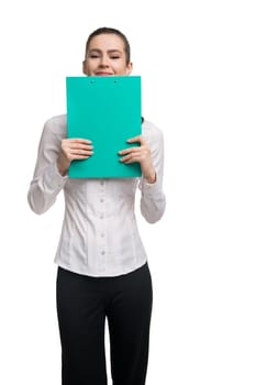Happy young lady in formal wear holding clipboard near face and smiling at camera during work against white background