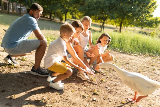 Family interacting with a goose in a sunny park