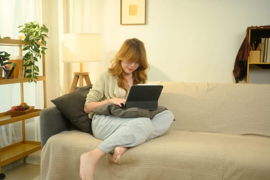Relaxed young woman using digital tablet for online learning or remote work at home.