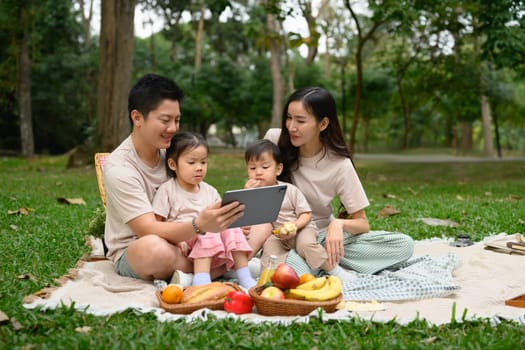 Happy family enjoys picnic in a beautiful park and watching something on digital tablet.