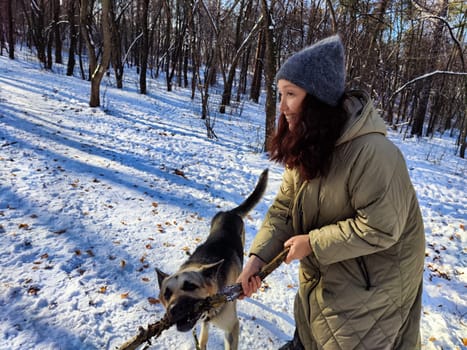 A girl and her German Shepherd dog explore a snowy forest, playing with a stick and enjoying the fresh winter air.
