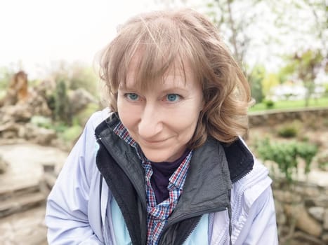 A middle-aged woman playfully takes selfies while exploring a lovely park during her trip, enjoying the natural surroundings.