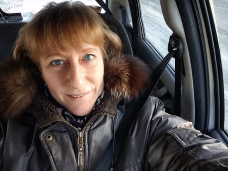 A middle-aged woman captures a selfie in her car, showcasing her excitement for a winter trip and the adventure ahead.