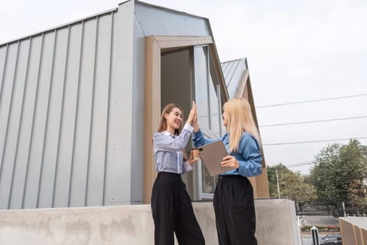 Two businesswomen outdoors giving each other a high-five, celebrating the success of their project while holding a tablet in a modern architectural setting.
