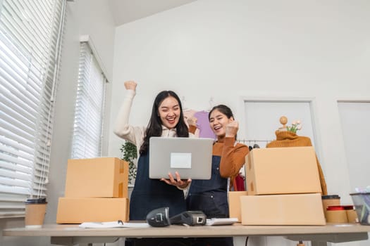 Two diverse retail workers cheerfully celebrating success together while managing inventory and using a laptop in a store environment.