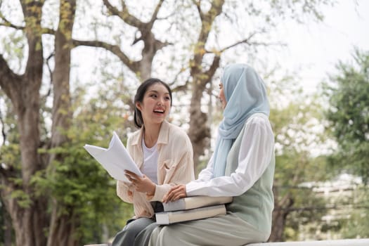 Diverse female students engaging in a lively discussion, holding books and notes while seated in a serene university park, sharing smiles and ideas.
