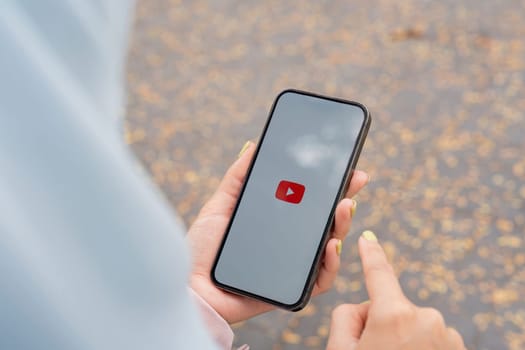CHIANG MAI, THAILAND - January 27,2025 : young woman holding smartphone hand is pressing the screen displays the Youtube app icons on Apple iPhone. YouTube is the popular online video-sharing website.