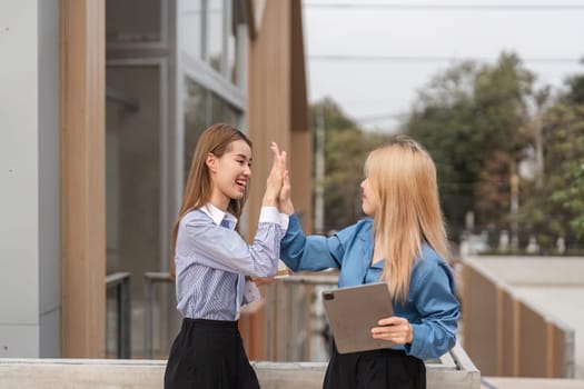 Two diverse women celebrating their success with a high-five while holding a tablet in an outdoor setting, showcasing joy and teamwork.