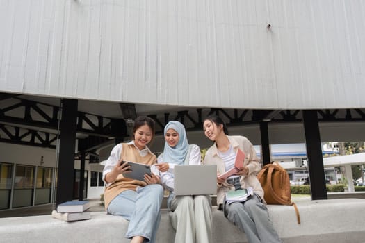 A group of multicultural female students sharing ideas and collaborating using a tablet and laptop, surrounded by books in a university campus environment.