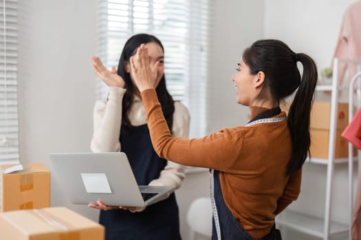 Two diverse female e-commerce employees high-fiving each other in celebration of success while working in a retail store setting.