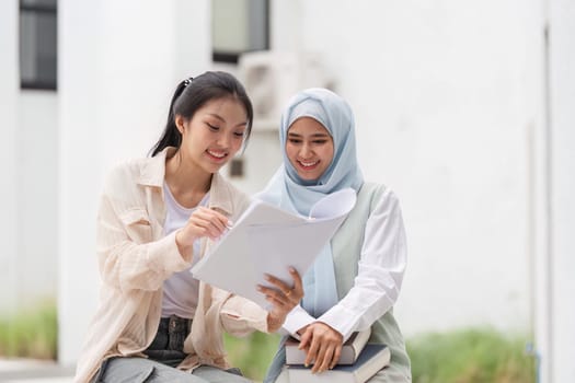 Two multicultural women engaged in a study session outdoors, sharing notes and discussing ideas in a friendly and collaborative atmosphere.