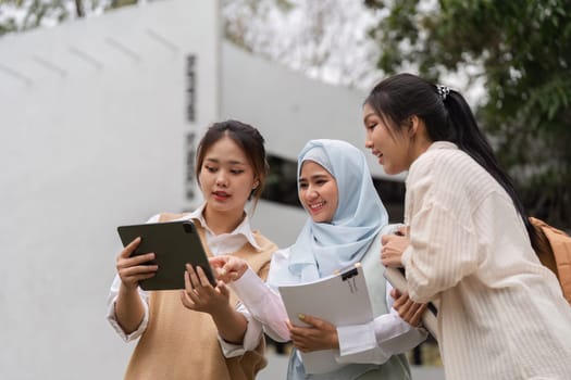 Three diverse female students collaborating around a tablet outdoors, sharing ideas and studying together in a vibrant academic environment.