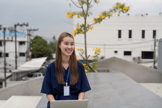 A relaxed female doctor in scrubs enjoys a moment of rest while using a laptop outdoors, highlighting the integration of technology and the importance of balance in her role