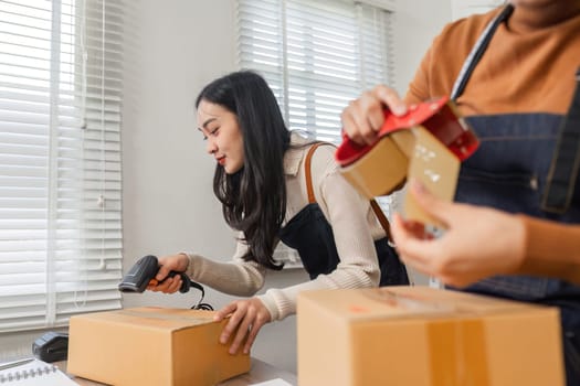 A diverse couple scanning packages with a barcode scanner while preparing online orders for shipment in their organized boutique workspace.