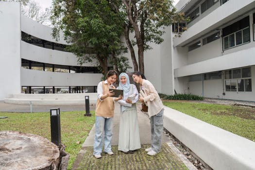 Three diverse multicultural women reviewing study materials together outdoors on campus, collaborating and sharing insights in a friendly academic environment.