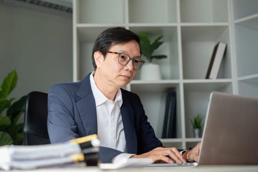 An elderly businessman focuses intently on digital tasks in a modern office setting showcasing dedication to his work.