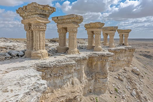 Weathered stone columns showcase ancient architecture in a vast desert area under clear skies.